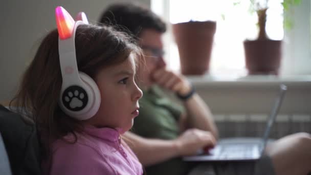 5岁的小女孩在沙发上玩电子游戏 而父亲在用笔记本电脑 高质量的4K镜头 — 图库视频影像