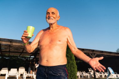 80 yaşında, sakallı, güneşli bir yaz gününde havuz kenarında dinlenen beyaz bir adam. Samimi yaşam tarzı, mutlu gerçek duygular. Yüksek kalite 4k görüntü