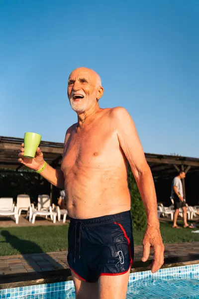 80 years old white man with beard relaxing near the pool on a hot summer sunny day. Lifestyle candid style, happy real emotions. High quality 4k footage