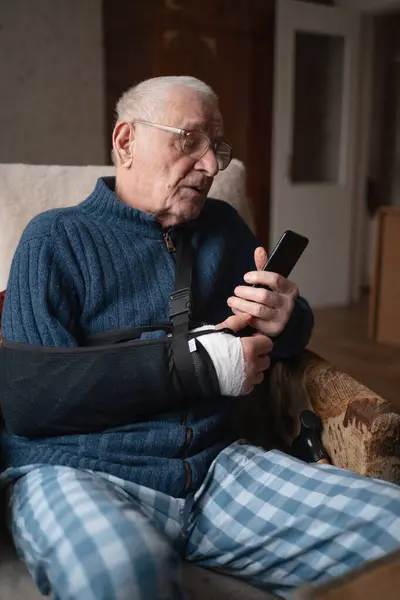 Senior with injured arm in sling browsing smartphone. High quality photo