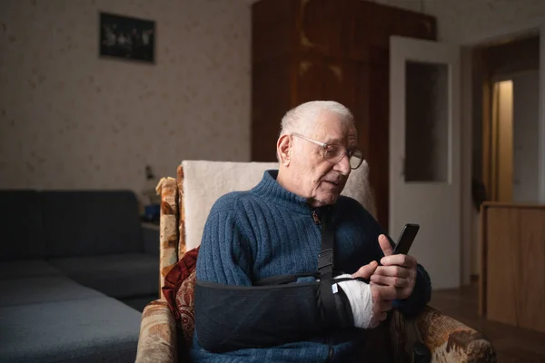 Senior with injured arm in sling browsing smartphone. High quality photo