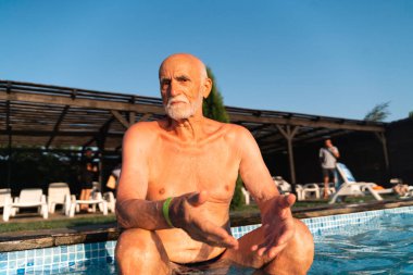 80 yaşında, sakallı, güneşli bir yaz gününde havuz kenarında dinlenen beyaz bir adam. Samimi yaşam tarzı, mutlu gerçek duygular. Yüksek kalite fotoğraf