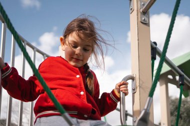 Kırmızı ceketli genç bir kız oyun parkındaki yapıya tırmanıyor ve oyun zamanını gösteriyor. Yüksek kalite fotoğraf