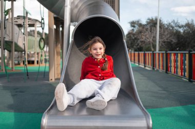 Mutlu bir çocuk oyun parkındaki kaydırağın tepesinde oturur, eğlenceye ve maceraya hazırdır. Yüksek kalite fotoğraf