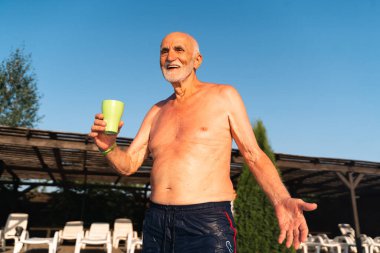 80 yaşında, sakallı, güneşli bir yaz gününde havuz kenarında dinlenen beyaz bir adam. Samimi yaşam tarzı, mutlu gerçek duygular. Yüksek kalite 4k görüntü