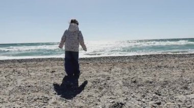 Çiçekli ceketli bir çocuk, macera ve keşif ruhunu somutlaştıran parıldayan okyanusa doğru yürür. Yüksek kalite 4k görüntü