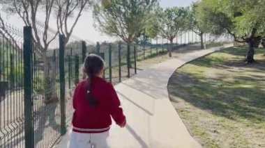 Genç bir kız ağaçlar ve çitlerle çevrili yemyeşil bir parkta dolambaçlı bir yolda sakin bir yürüyüş yapar. Yüksek kalite 4k görüntü