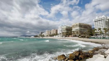 Dinamik gökyüzü altında geniş açılı deniz manzarası, bereketli palmiye ağaçları tarafından çevrelenmiş ve Akdeniz tarafından çerçevelenmiş. Yüksek kalite 4k görüntü