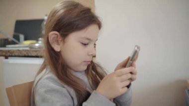 Odaklanmış genç bir kız akıllı telefonuyla modern çocukların teknolojiyle etkileşimini gösteriyor. Yüksek kalite 4k görüntü