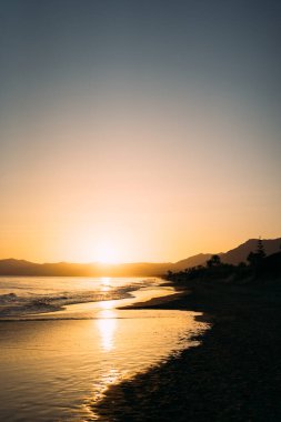 Güneş ufkun altına batıyor, sakin sahil manzarasına huzur verici bir altın rengi yansıtıyor, huzurlu bir tefekküre davetiye çıkarıyor. Yüksek kalite fotoğraf