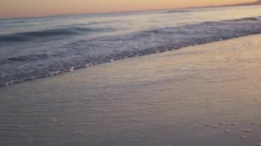 Yumuşak dalgalar, altın saat boyunca sıcak, pastel bir gökyüzünün altında kumlu sahili okşayarak sakin bir günbatımı sahnesi yaratır. Costa Del Sol, İspanya, Endülüs, Marbella. Yüksek kalite 4k görüntü