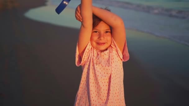 一个笑容满面的小女孩在夕阳西下的海滩上拿着一只蓝色的水桶 展示着童年时代的欢乐和欢乐 高质量的4K镜头 — 图库视频影像