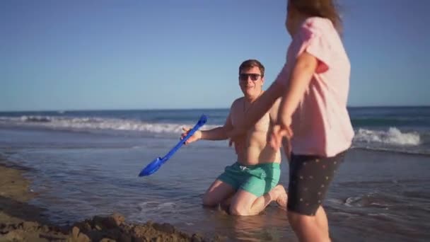 一个赤身裸体的男人笑着和一个孩子玩耍 在阳光灿烂的海岸线上玩海滩玩具 高质量的4K镜头 — 图库视频影像
