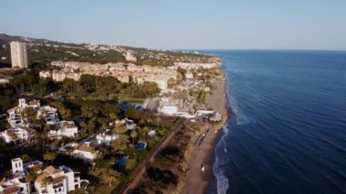 Gün batımının sıcacık parıltısının altında masmavi denizle buluşan şehir manzarasının kuşbakışı görüntüsü. Costa Del Sol, Marbella, Endülüs, İspanya, Las Chapas Dunes. Yüksek kalite 4k görüntü