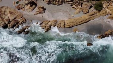 Çarpıcı bir hava manzarası, okyanus dalgalarının doğal güzelliğini ve ham gücünü yakalıyor ve engebeli bir kayalık sahil şeridine çarpıyor, Playa de Cala Sardina.
