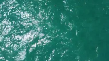 Okyanusun canlı turkuaz sularını beyaz köpük ve dalgaların yavaşça yüzeye yayıldığı bir hava görüntüsü. Yüksek kalite 4k görüntü