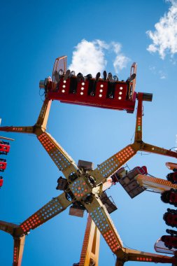 Aşağıdaki insanların, açık mavi bir arkaplanı olan bir panayırda eğlenceli bir gezintinin keyfini çıkardıkları bir manzara. Yüksek kalite fotoğraf