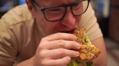 Gözlüklü ve taze, ev yapımı bir sandviç yiyen bir adamın yakın çekimi. Yüksek kalite 4k görüntü