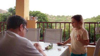 Bir baba ve kızı, dışarıdaki bir masada manzaralı arka planda oyuncak modeller yapmaya odaklanmış. Yüksek kalite 4k görüntü