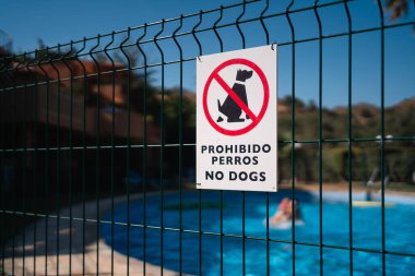 Bir havuzu çevreleyen çitin üzerinde İspanyolca ve İngilizce 