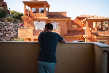 Bir adam renkli binalar ve güneşli bir gökyüzüyle çevrili balkonundan kentsel manzarayı izliyor. Yüksek kalite fotoğraf