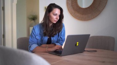  Mavi kot gömlekli bir kadın dizüstü bilgisayarı üzerinde çalışırken gülümsüyor ve işinden zevk alıyor. Yüksek kalite 4k görüntü