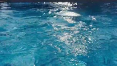 Açık mavi bir su yüzeyindeki dalgalanmalar, sakin ve huzurlu bir sahnede güneş ışığını yansıtıyor. Yüksek kalite 4k görüntü