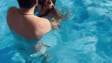 Genç bir kız babasıyla açık havuzda yüzerken su sıçratır. Güneş altında eğlenceli bir günün tadını çıkarırlarken kız gözlük takıyor ve gülümsüyor. Yüksek kalite fotoğraf