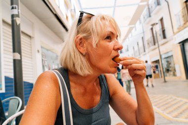 A mature woman indulging in local street food at an outdoor cafe in Ronda, Spain, enjoying the culinary delights during her trip. High quality photo clipart