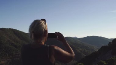Malaga, Endülüs 'te bir tepede duran bir kadın, altın saatinde manzaranın fotoğrafını çekmek için akıllı telefonunu kullanıyor. Yüksek kalite 4k görüntü