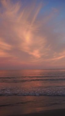 Yumuşak pembe ve turuncu bir gökyüzünün yer aldığı güzel bir sahil gün batımı sakin okyanus dalgalarını yansıtarak barışçıl bir atmosfer yarattı. Yüksek kaliteli FullHD görüntüler