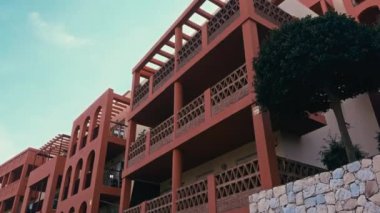 Terracotta apartmanı, dekoratif balkonlar ve geometrik detaylarla dolu, temiz bir gökyüzüne karşı kurulmuş, sıcak, Akdeniz mimarisini çağrıştırıyor. Yüksek kalite 4k görüntü