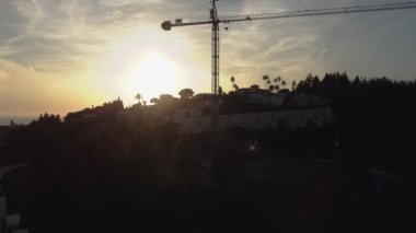  Gün batımında siluetli inşaat vinci, banliyö manzarasında evler ve ağaçlarla çevrili. Yüksek kalite 4k görüntü