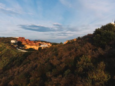 A scenic view of Calahonda, near Marbella, with residential buildings on a hillside under a sky filled with sunset clouds, capturing a peaceful coastal ambiance. High quality photo clipart