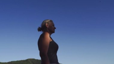  Bir kadın, parlak mavi gökyüzünün altındaki yemyeşil bir dağ manzarasına bakar. Doğanın güzelliğine minnettarlığını gösterir. Yüksek kalite fotoğraf