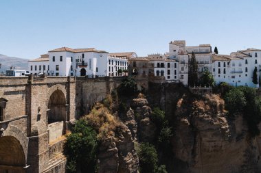 İspanya, Ronda 'nın panoramik manzarasında açık mavi gökyüzünün altında dramatik uçurumlara tünemiş ikonik Puente Nuevo köprüsü ve büyüleyici beyaz boyalı binalar görülüyor. Yüksek kalite fotoğraf