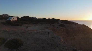 Portekiz, Algarve 'nin engebeli uçurumlarında tek başına duran gezgin engin okyanus ufkunun üzerinde sakin günbatımını seyrediyor. Yüksek kalite 4k görüntü