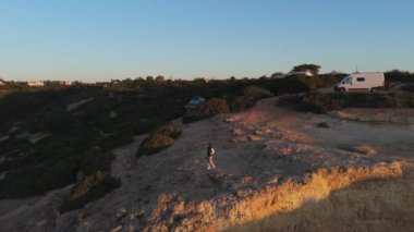 Kamp arabaları ve Algarve günbatımının tadını çıkaran yalnız bir gezginin olduğu manzaralı bir uçurum kenarı. Doğa ve macerayı ön plana çıkarıyor. Yüksek kalite 4k görüntü