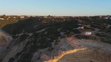 Minibüsler ve Algarve uçurumlarına bakan gezginlerle dolu bir sahil kamp alanı. Yüksek kalite 4k görüntü