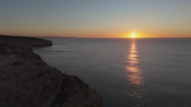 Gün batımında sersemletici Algarve uçurumları. Sakin okyanuslar, insansız hava araçları tarafından çekilen altın renkleri yansıtıyor. Nefes kesici ve sakin bir sahil manzarası. Yüksek kalite 4k görüntü