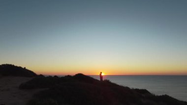 Algarve 'da gün batımı manzarası göz kamaştırıcı, okyanusa bakan siluetli bir figür. Yavaş yaşam ve maceralı van hayat tecrübeleri için mükemmel. Yüksek kalite 4k görüntü