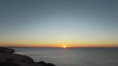 Portekiz 'in Praia de Carvalho yakınlarındaki Algarve kıyı şeridi boyunca sakin okyanus sularını aydınlatan altın bir gündoğumu barış ve yenilenmeyi simgeliyor. Yüksek kalite 4k görüntü