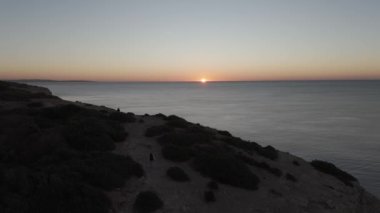 Portekiz, Carvoeiro yakınlarındaki engebeli Algarve kayaları üzerinde tripodunu kuran yalnız bir kadın içerik yaratıcısı güneşin doğuşunu ve Atlantik Okyanusu 'nun güzelliğini yakalıyor. Yüksek kalite 4k görüntü