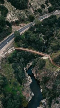 Benahavis, Endülüs, İspanya 'daki Guadalmina Nehri yakınlarındaki yemyeşil ve engebeli manzaralarla çevrili bir kanyonu aşan ahşap bir köprünün havadan görünüşü. Yüksek kalite 4k görüntü