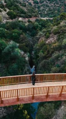 Bir gezgin Benahavis, Endülüs, İspanya 'da yeşil manzaralar ve engebeli kaya oluşumlarıyla çevrili manzaralı bir kanyon boyunca uzanan tahta bir köprüde durur. Yüksek kalite 4k görüntü