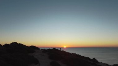 Algarve 'da gün batımı manzarası göz kamaştırıcı, okyanusa bakan siluetli bir figür. Yavaş yaşam ve maceralı van hayat tecrübeleri için mükemmel. Yüksek kalite 4k görüntü