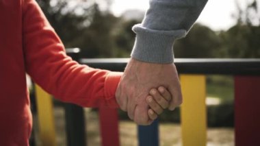 Parkta çok renkli bir çitin yanında bir yetişkinin elini tutan bir çocuğun yakın çekimi bakım ve güveni sembolize ediyor. Yüksek kalite 4k görüntü