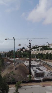 Ağaçlar ve kentsel binalarla çevrili vinçlerle ve işçilerle dolu büyük bir inşaat alanının havadan görüntüsü. Yüksek kalite 4k görüntü