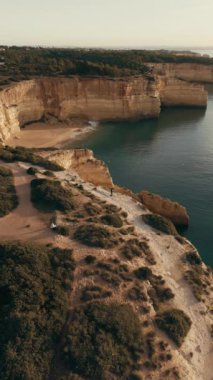 Yukarıdan çekilen resimli kıyı şeridi altın plajları, engebeli uçurumları ve Benagil ve Praia do Carvalho yakınlarındaki manzaralı yürüyüş yollarını gözler önüne seriyor. Yüksek kalite 4k görüntü