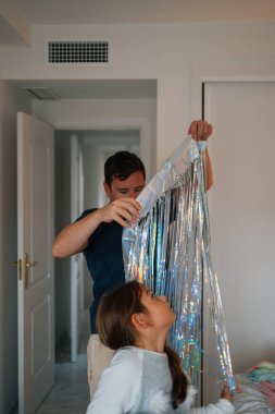 Beyaz bir baba ve genç bir kız yatak odasında parlak flamalarla dekore ediyorlar..